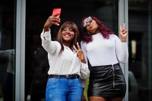 Two female friends african american models posed outdoor with mobile phone at hand. photo