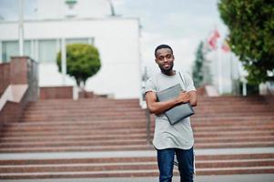 African student male posed with backpack and school items on yard of university, against flags of different countries. photo