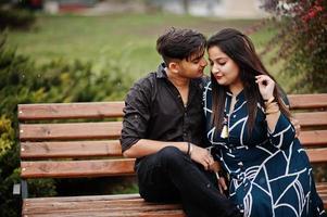 Love story of indian couple posed outdoor, sitting on bench together. photo