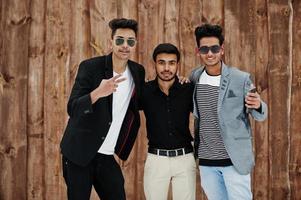 Group of three casual young indian mans posed against wooden background. photo