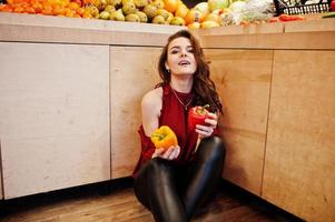 chica de rojo sosteniendo dos pimientos en la tienda de frutas. foto