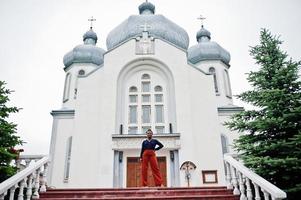 African woman in orange pants and blue shirt posed against large church. Faith and believe on God. photo