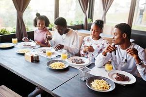 felices amigos africanos sentados, charlando en un café y comiendo. grupo de personas negras reunidas en un restaurante y cenando. foto