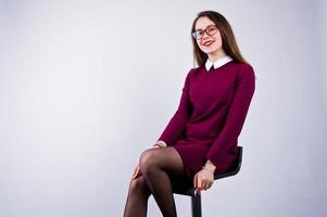 retrato de una mujer joven con vestido morado y gafas sentada en la silla del estudio. foto