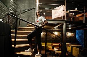 Stylish african american woman in printed t-shirt posed indoor steel stairs. photo