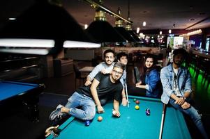 Group of stylish asian friends wear on jeans playing pool billiard on bar. photo