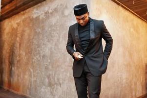 Strong powerful african american man in black suit and turtleneck and cap, with elephant tusk. photo