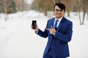 Stylish indian business man in suit and glasses posed at winter day outdoor, with mobile phone at  hand. photo