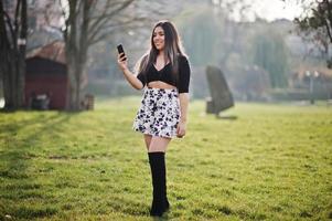 Pretty latino model girl from Ecuador wear on black tops and skirt posed at street with mobile phone. photo