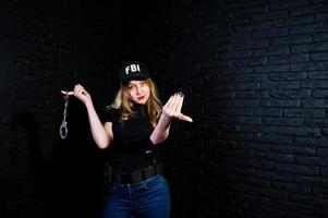 FBI female agent in cap and with gun at studio against dark brick wall. photo