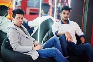 Two asian guys sitting on poufs at play room against mirror. photo