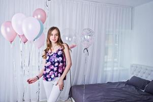 Happy girl with colored balloons on bed at room. Celebrating birthday theme. photo