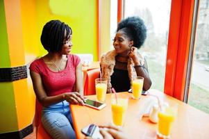 Two young african girls with juices sitting in bright colored fast food restaurant. photo