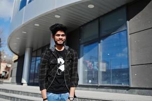 hombre asiático con barba en ropa informal posando contra un nuevo edificio moderno. foto