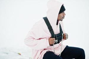 Elegante hombre afroamericano de estilo urbano con capucha rosa posado en un lago congelado en invierno. foto