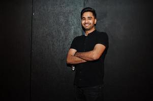 Asian man in black shirt on dark background posed with crossed arms. photo