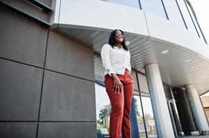 Formally dressed african american business woman in white blouse and red trousers. Successful dark skinned businesswoman.