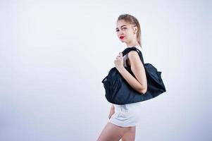 Amazing fit sexy body brunette caucasian girl posing at studio against white background on shorts and top with black sport bag. photo