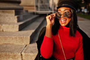 African american fashion girl in coat and newsboy cap, sunglasses posed at street. photo