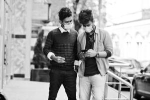 Coronavirus covid-19 concept. Two south asian indian man wearing mask for protect from corona virus looking at mobile phone. New normal lifestyle post pandemic in India. photo