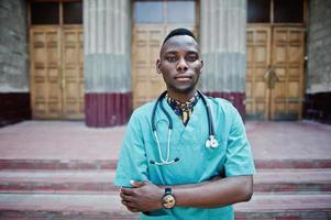 African american doctor male at lab coat with stethoscope outdoor against clinic door. photo