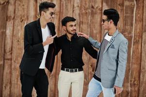 Group of three casual young indian mans posed against wooden background. photo