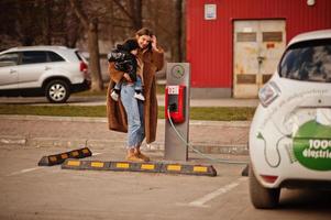 joven madre con niño cargando electro coche en la gasolinera eléctrica. foto