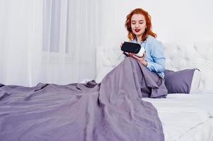 Red haired girl in bed with vr glasses at studio room. photo