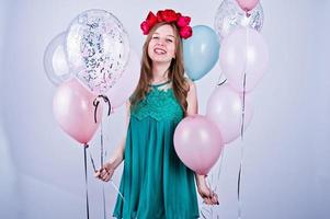 chica feliz con vestido verde turquesa y corona con globos de colores aislados en blanco. celebrando el tema del cumpleaños. foto