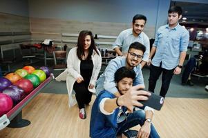 Group of five south asian peoples having rest and fun at bowling club. Making selfie by phone. photo