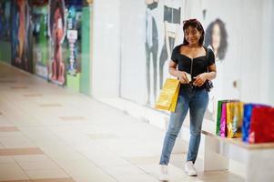 African-american woman walking with coloured shopping bags in mall shopping center and speak by phone. photo