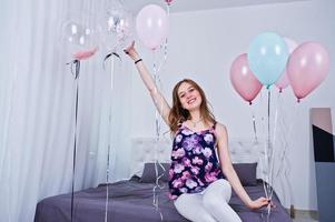 Happy girl with colored balloons on bed at room. Celebrating birthday theme. photo