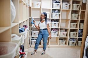 Cheerful african american woman with iron at hand in the self-service laundry. photo