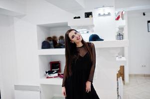 hermosa chica morena en la boutique de la tienda de ropa en vestido negro. foto