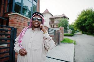 Middle Eastern arab business man posed on street against modern building with sunglasses, speaking on mobile phone. photo