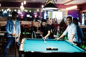 Group of stylish asian friends wear on jeans playing pool billiard on bar. photo