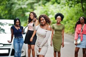 Group of five happy african american girls posed against car, one of them show keys. photo