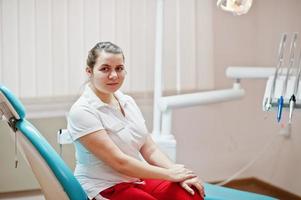 retrato de mujer dentista de pie en su oficina de odontología sentada en una silla. foto