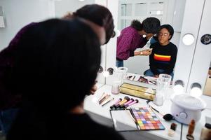 African American woman applying make-up by make-up artist at beauty saloon. photo