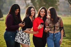 Group of four happy and pretty latino girls from Ecuador posed at street and looking at mobile phones. photo