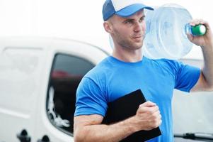 Delivery man with clipboard in front cargo van delivering bottles of water. photo