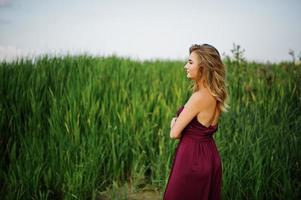 Blonde sensual woman in red marsala dress posing in the reeds. photo