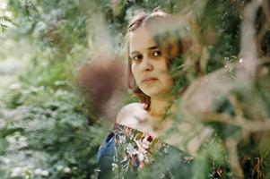 Close-up portrait of a beautiful brunette in dress next to the leaves. photo