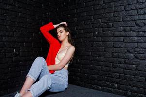 chica morena con estilo en chaqueta roja contra la pared de ladrillo negro de estudio. foto