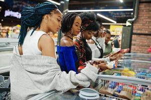 Group of african womans with shopping carts near refrigerator choose packs of dumplings in the supermarket. photo