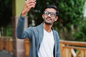 un hombre indio elegante con anteojos usa una pose informal al aire libre y se hace selfie por teléfono. foto