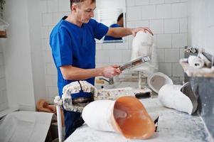 hombre protésico que hace prótesis de pierna mientras trabaja en laboratorio, hace un modelo de yeso. foto