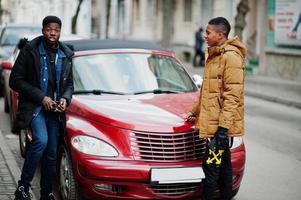 Two african male friends standing near red american convertible car. photo