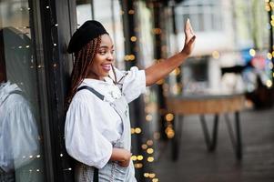 African american woman in overalls and beret posed in outdoor terrace with christmas decorations garland. photo