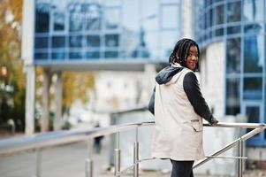 Attractive african american woman with dreads in jacket posed near railings against modern multistory building. photo